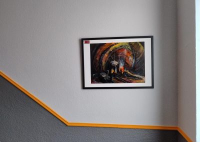 Abstrakte Kunst mit kräftigen Farben in einem Rahmen an einer Wand im Treppenhaus.