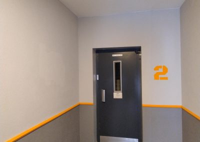 Schwarze Tür mit einem Fenster und der Nummer 2 an der Wand im Flur.